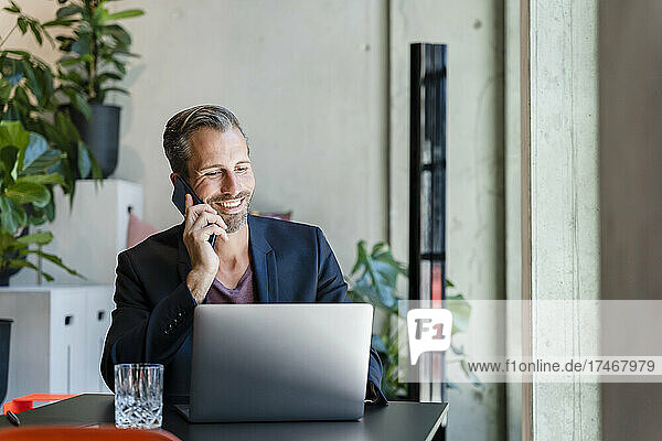 Smiling businessman using laptop while talking on phone in office