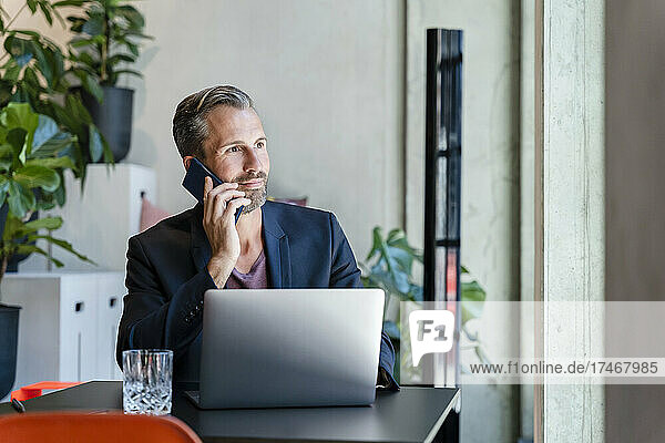Businessman with laptop talking on smart phone in office
