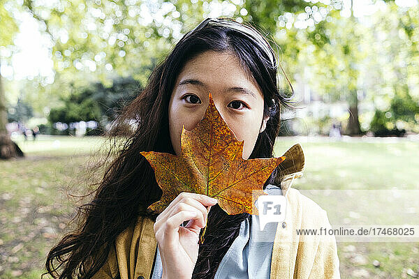 Woman covering mouth with maple leaf in park