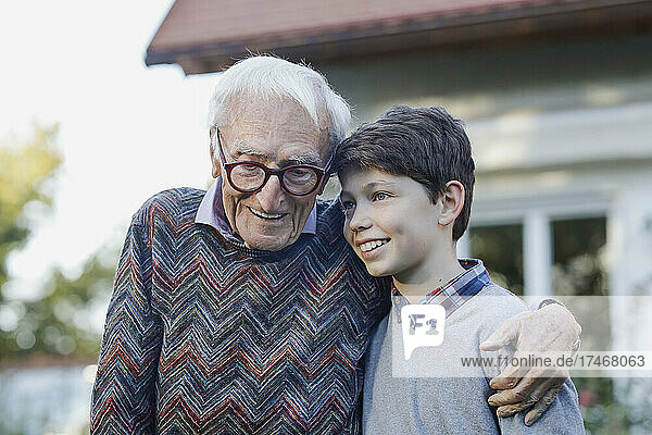 Smiling senior man with arm around of grandson in backyard