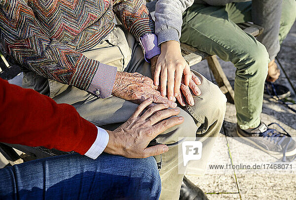 Affectionate boy and father touching hands of grandfather in backyard