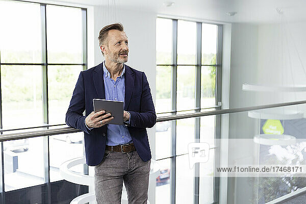 Male professional standing with digital tablet at corridor in office