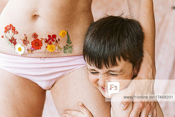 Glücklicher Sohn umarmt Mutter mit Blumentattoo auf Kaiserschnittnarbe