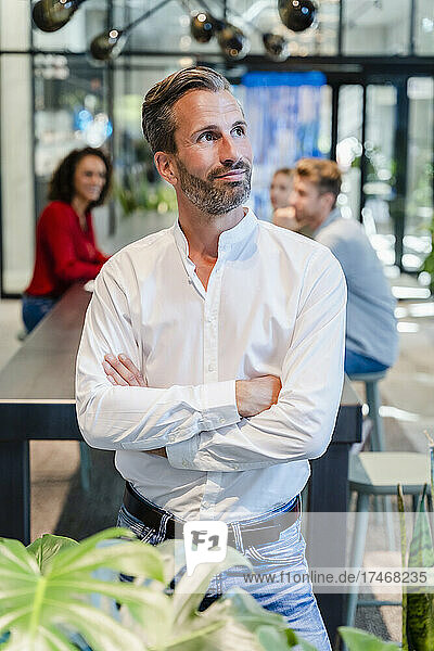 Thoughtful businessman with arms crossed in coworking office