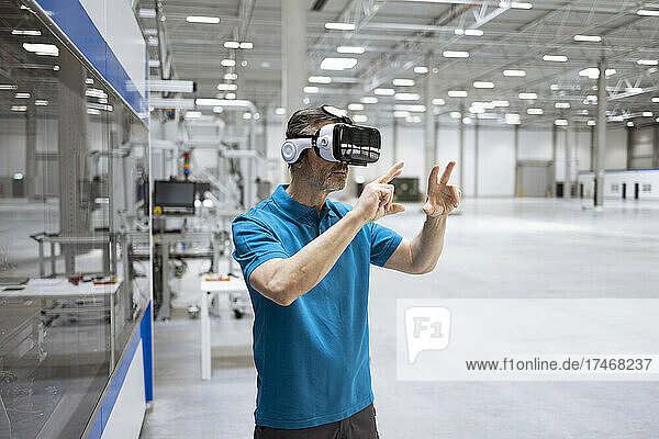 Male professional gesturing while using virtual reality headset in factory