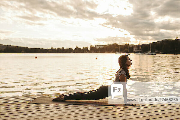 Woman practicing yoga on jetty by lake during sunset