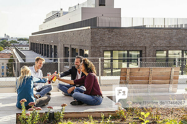 Happy colleagues toasting bottle while sitting on terrace