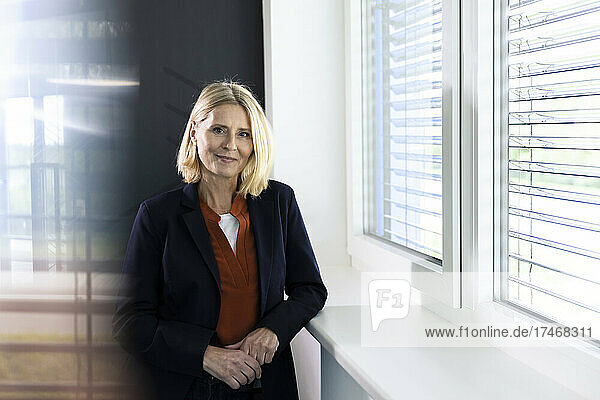 Smiling mature businesswoman standing by window in office