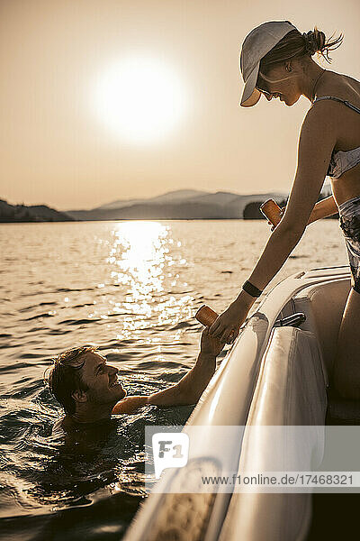 Woman giving drink to man swimming in lake at sunset