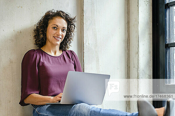 Smiling businesswoman with laptop on lap at office