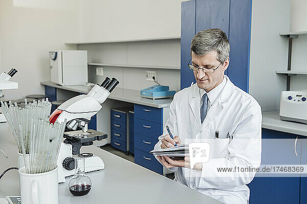 Scientist with eyeglasses writing in note pad at laboratory