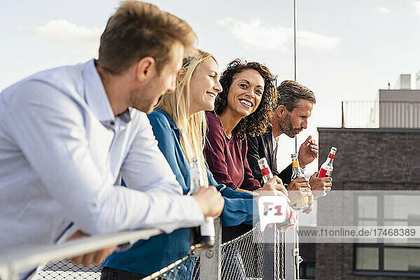 Colleagues having drink while leaning on terrace railing