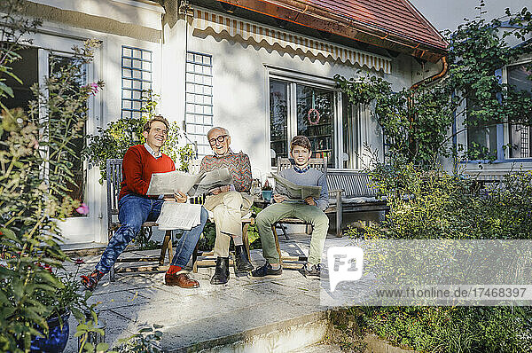 Glückliche Familie mit Zeitung  die auf einem Stuhl im Hinterhof sitzt