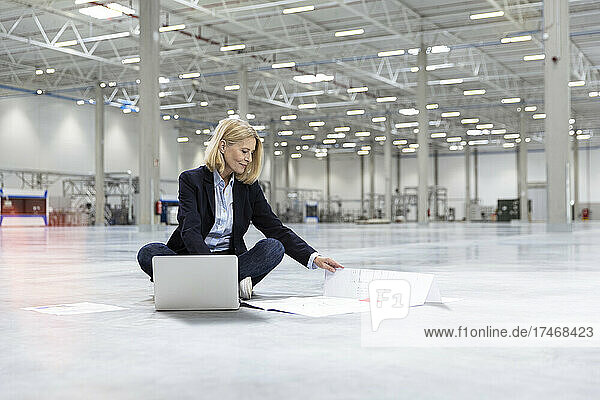 Businesswoman sitting with laptop and blueprint in industry