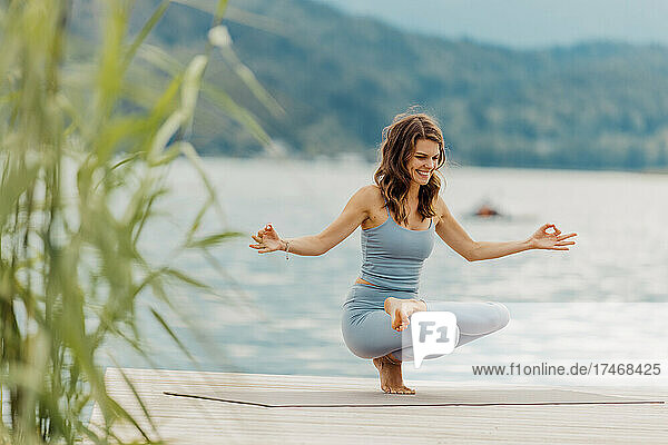 Glückliche Frau macht Yoga auf dem Steg am See