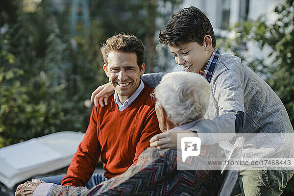 Smiling boy with father looking at grandfather in backyard