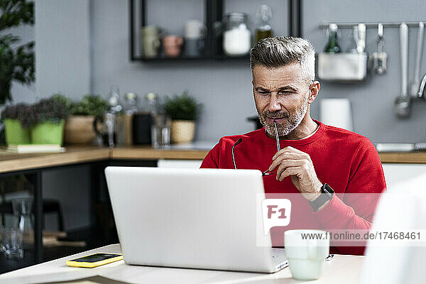Man holding eyeglasses while using laptop at home