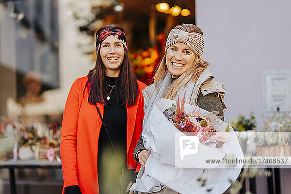 Happy woman with flowers by friend in front of shop