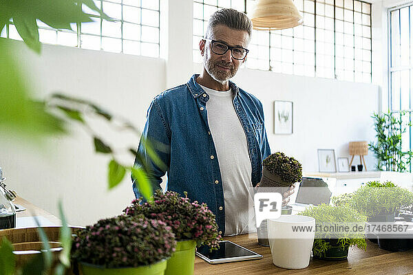 Mature man with potted plant standing at home