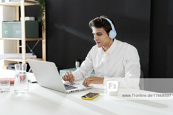 Businessman wearing headphones working on laptop at desk in office