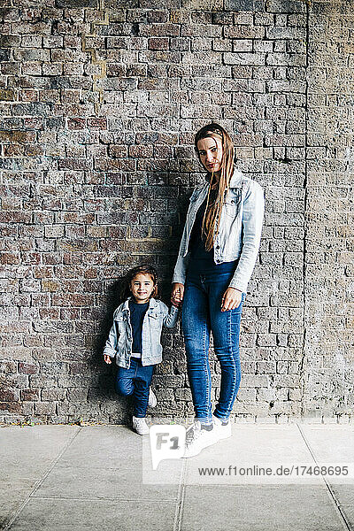 Mother and daughter standing together in front of brick wall
