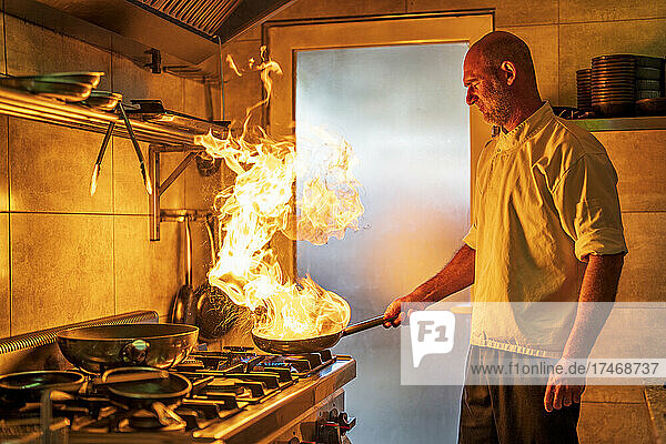 Male chef with flaming pan cooking in kitchen