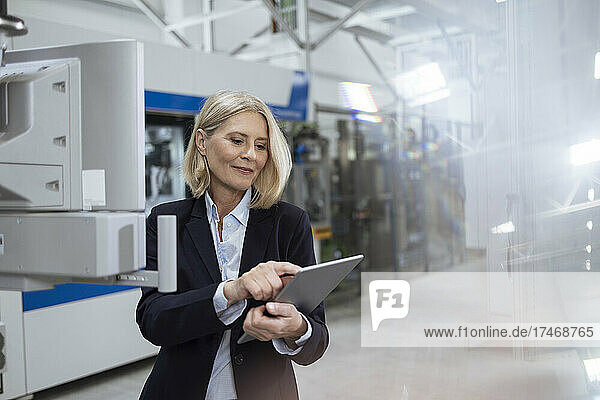 Smiling female professional using digital tablet by machinery in factory