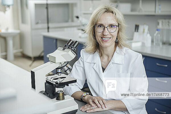 Smiling blond researcher with microscope in laboratory