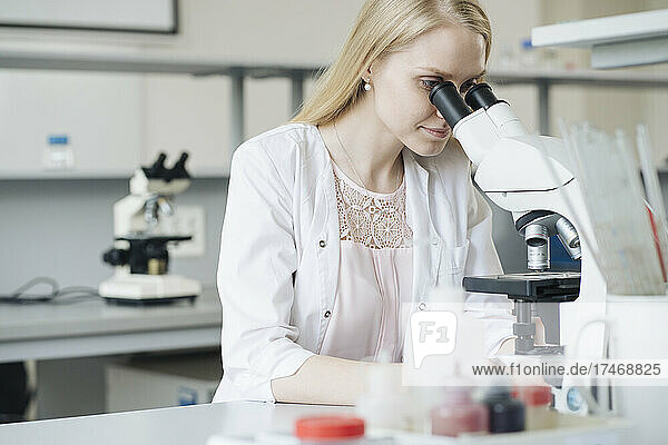 Blond female scientist researching through microscope in laboratory