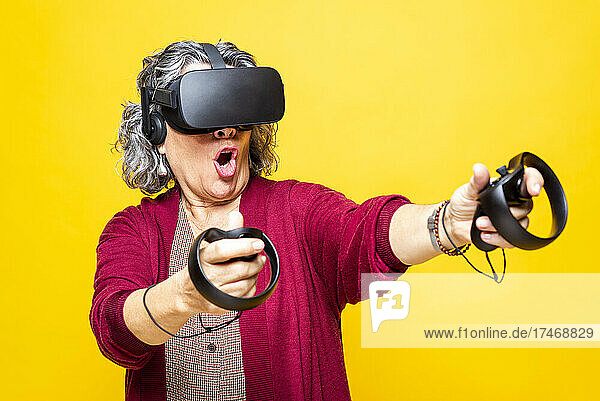 Woman holding joystick while wearing virtual reality headset against yellow background