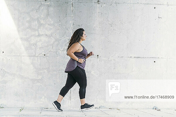 Young plus size sportswoman running on footpath