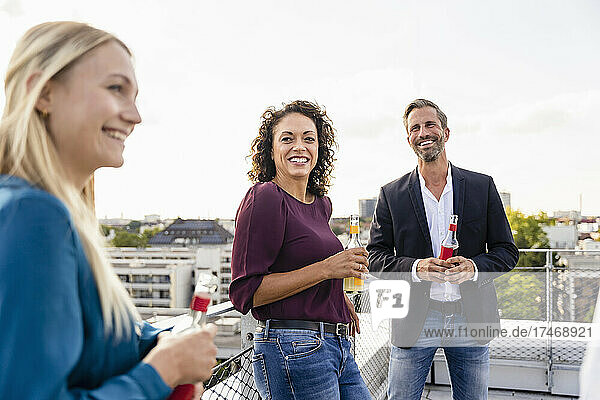 Smiling businesswoman holding alcohol bottle with colleagues on rooftop