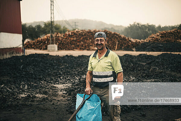 Smiling worker with plastic bag and tool standing at coal factory