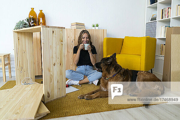 Smiling woman with dog having coffee in living room