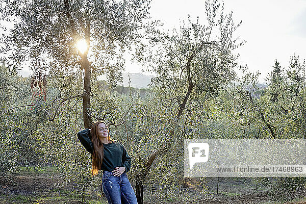 Lächelnde Frau lehnt bei Sonnenuntergang an einem Olivenbaum