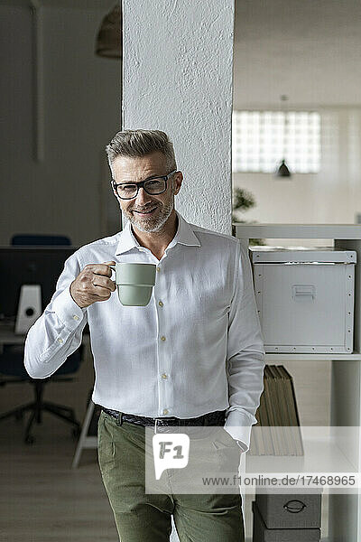 Lächelnder Geschäftsmann hält Kaffeetasse im Büro