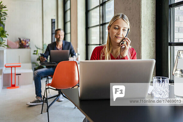 Geschäftsfrau benutzt Laptop  während sie im Büro mit dem Mobiltelefon telefoniert