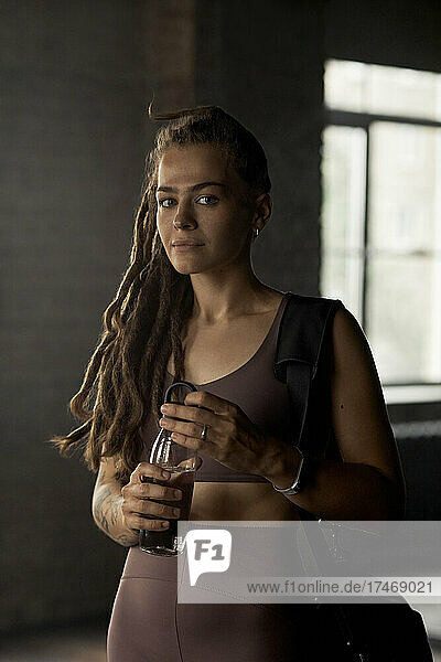 Young sportswoman with locs hairstyle holding water bottle