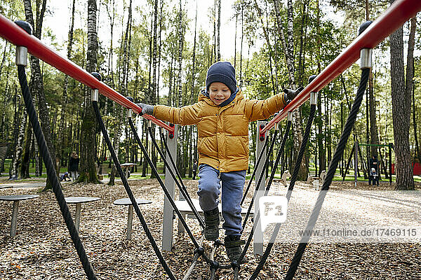 Boy walking on play equipment at park during autumn