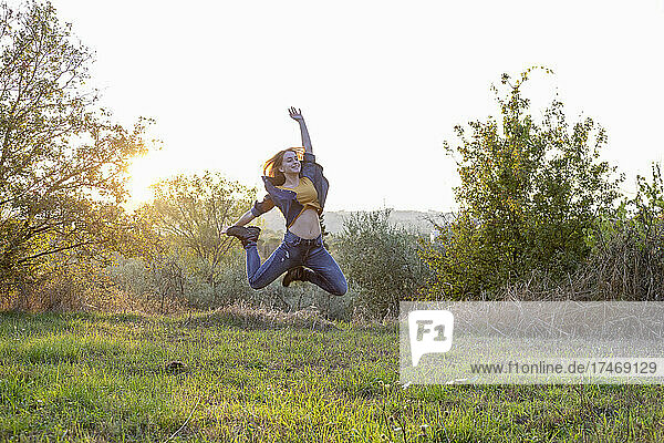 Carefree woman jumping over grass at sunset
