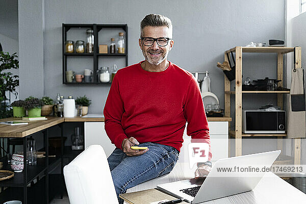 Smiling mature man with laptop and smart phone sitting on table
