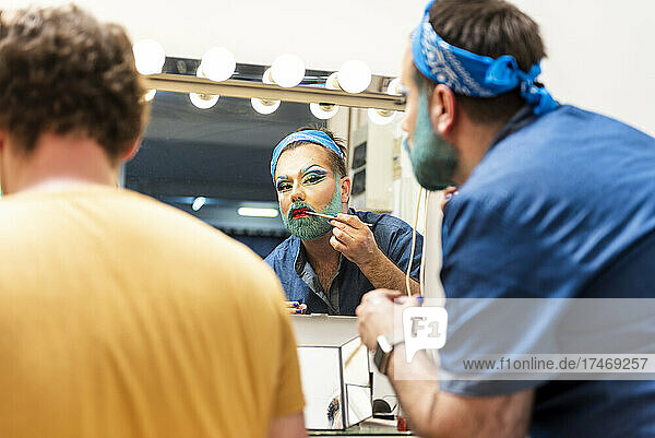 Bearded man doing drag queen makeup by friend