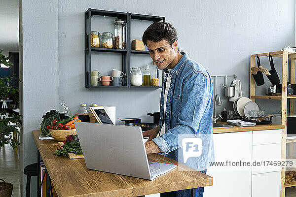 Smiling man using laptop in kitchen at home