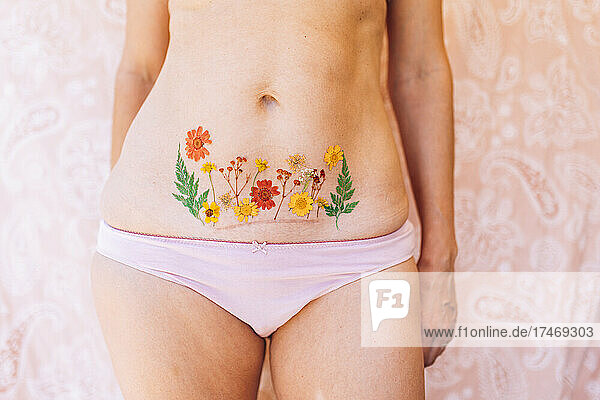 Woman in underwear showing Caesarean scar with flowers tattoo