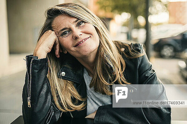 Smiling mature woman wearing leather jacket sitting at sidewalk cafe