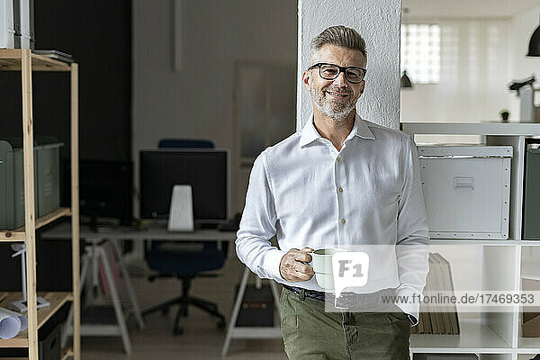 Smiling businessman with coffee mug leaning on architectural column