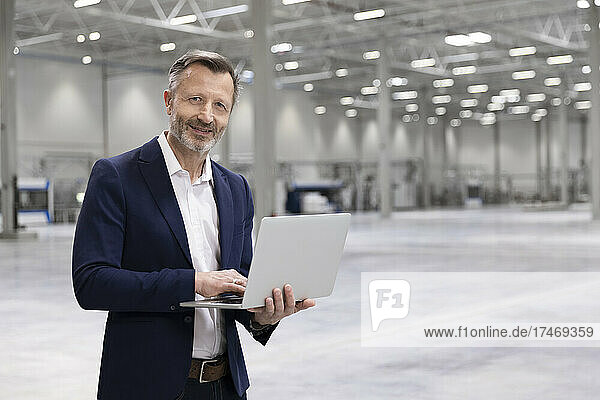 Mature businessman with laptop smiling in industry