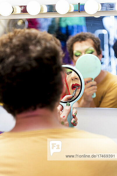 Mann mit Spiegel schminkt sich in der Umkleidekabine