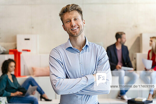 Smiling young businessman with arms crossed in office