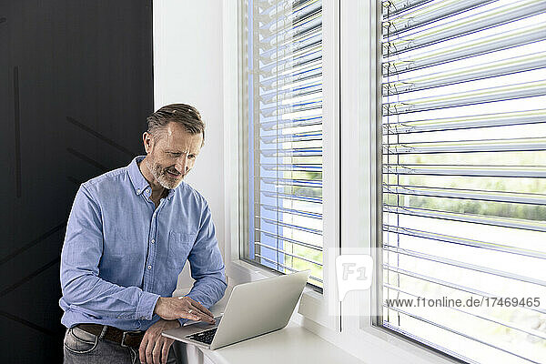 Businessman working on laptop by window in office